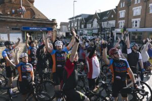 Cyclists taking part in Ride 1000 and their friends and family cheer and wave outside Southfields Undergound Station before setting off